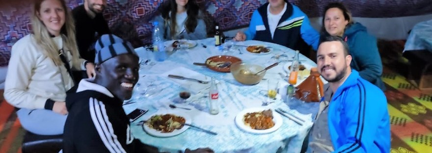 Los viajeros alrededor de la mesa están degustando la gastronomía senegalesa en una haima