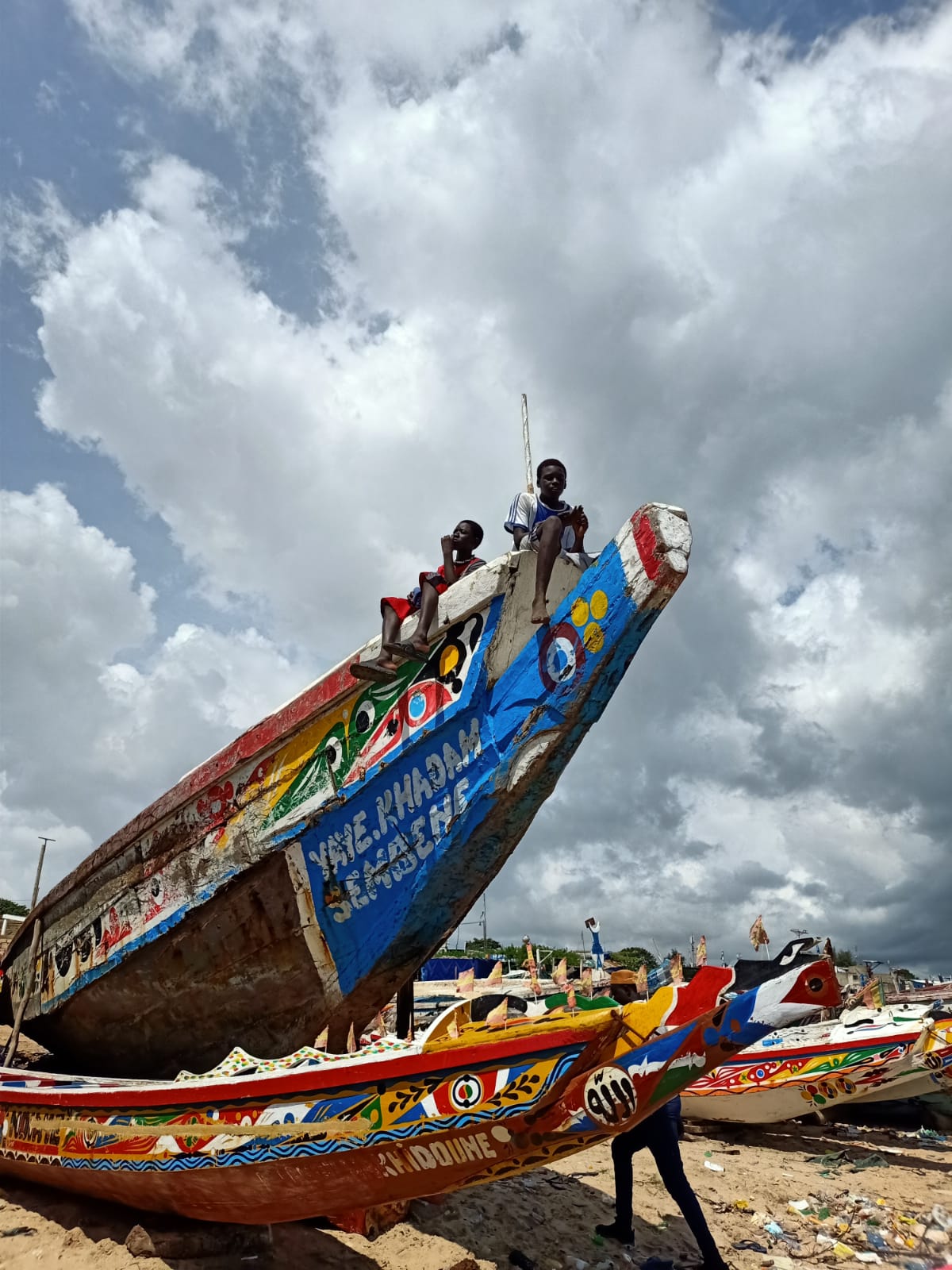 Barcos pesqueros tradicionales de colores brillantes a la orilla del mar, niños subidos en su proa