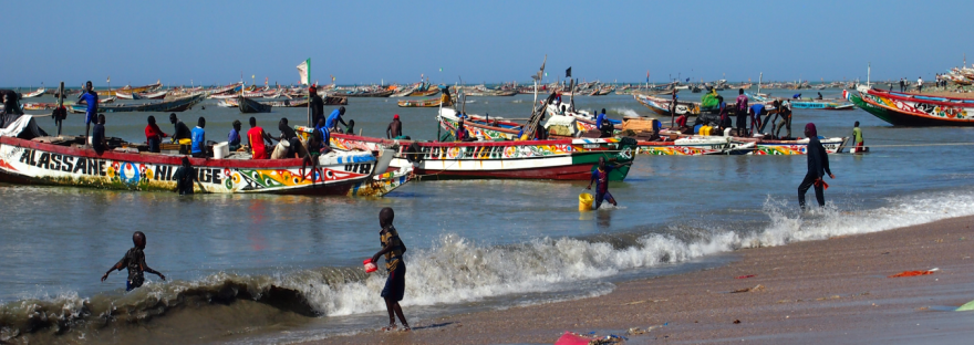 Barcos de colores en el mar y los niós en la orilla, estampas del puerto de Mbour